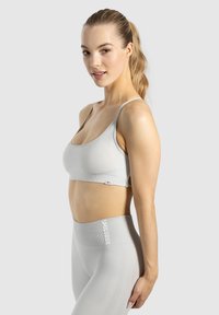 Helle graue Sport-BH mit dünnen Trägern und einem taillierten Design. Schlichte Textur, minimale Markierung, kombiniert mit passenden hochgeschnittenen Leggings.