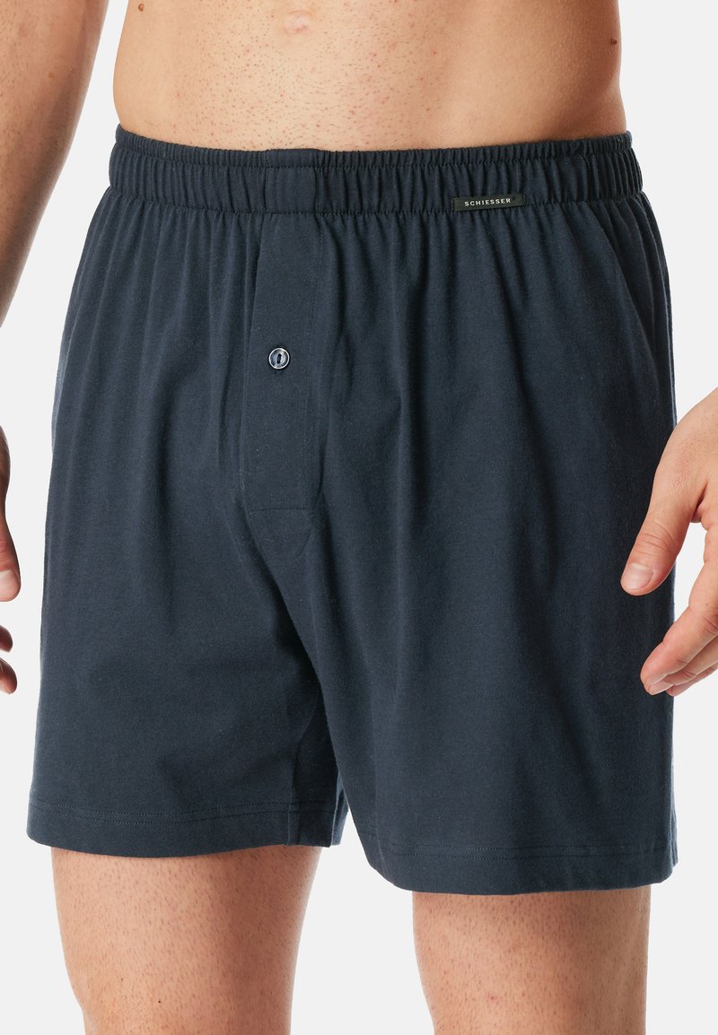 Boxer in cotone blu navy con vita elastica, apertura con bottone e dettagli di cucitura minimi. Tessuto morbido con vestibilità rilassata.