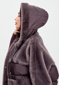 Pružná bunda v tmavě růžové barvě s umělou kožešinou na kapuci, vybavená zipovým uzávěrem, v oversize designu a podšitá pro lepší izolaci.