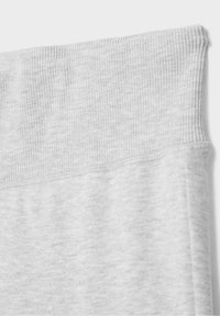 Gros plan sur un tissu gris clair montrant une ceinture côtelée et une texture tricotée douce sur un pantalon ou un legging.