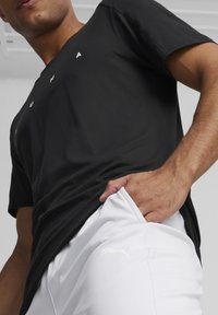 Camiseta atlética negra de manga corta con letras blancas, combinada con pantalones cortos blancos que presentan un sutil logotipo de Puma en el bolsillo. Textura suave.