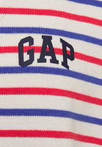 Pruhovaný bavlněný svetr s červenými, modrými a bílými vodorovnými pruhy a námořnicky modrým logem "GAP" na hrudi. Měkká pletená textura.