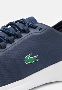 Navy athletic shoe with textured upper, rubber sole, and distinctive green crocodile logo. Features braided laces and padded tongue.