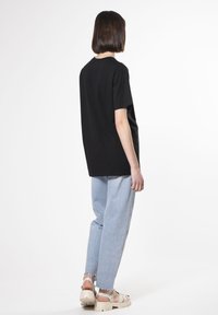 Camiseta de algodón negra de manga corta, combinada con jeans de denim azul claro y sandalias de plataforma beige. Diseño sencillo y de corte relajado.