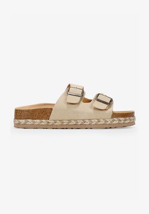 Beige Wildleder-Slides mit zwei verstellbaren Riemen und metallischen Schnallen, einer Korksohle und einer gewebten Juteverzierung um die Basis.