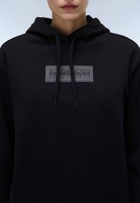Svart hettegenser laget av myk stoff, med et sentralt grått logo-patch med "NAPAPIJRI" tekst og snorhette.
