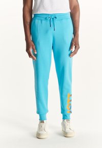 Lichtblauwe sweatpants met een elastische tailleband, zijzakken en een contrasterend oranje logo bedrukt op het onderste deel van het linkerbeen.