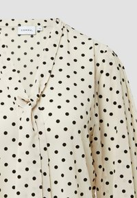 Cremfarbene Bluse mit schwarzen Punkte, V-Ausschnitt mit Bindeband und leicht gepufften langen Ärmeln.