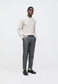 Hellgraues, geripptes Langarmshirt kombiniert mit dunkel gestreiften, vertikal gemusterten Hosen. Schwarze Slipper mit cremefarbenen Akzenten.