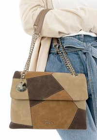Bruine en beige suède handtas met geometrisch patchworkontwerp, voorzien van een kettingriem, een ronde metalen tag en een klepafsluiting.