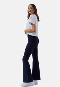 Biała krótka koszulka, granatowe rozszerzane spodnie, zestawione z białymi trampkami. Gładki materiał, dopasowany krój, widok z boku podkreślający kształt stroju.