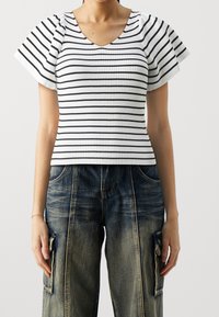 Top blanco de canalé con rayas negras horizontales y mangas acampanadas, combinado con pantalones cargo de denim oscuro de corte holgado con bolsillos laterales.