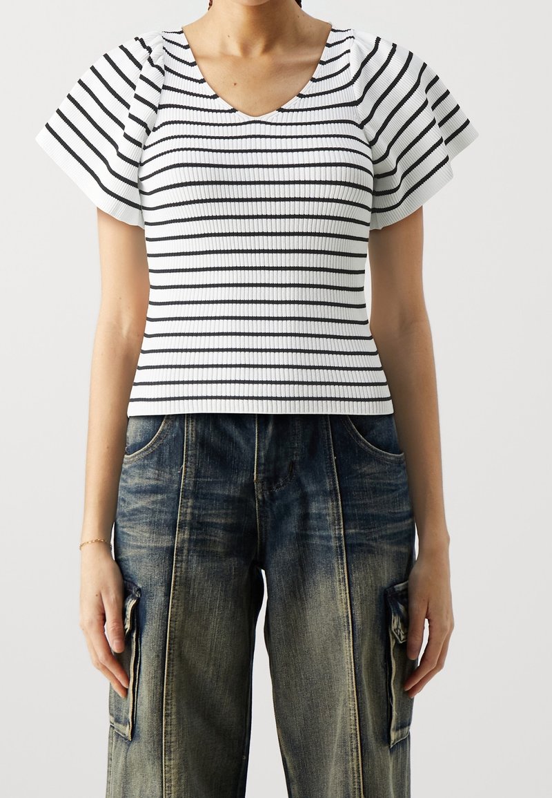 Top blanco de canalé con rayas negras horizontales y mangas acampanadas, combinado con pantalones cargo de denim oscuro de corte holgado con bolsillos laterales.