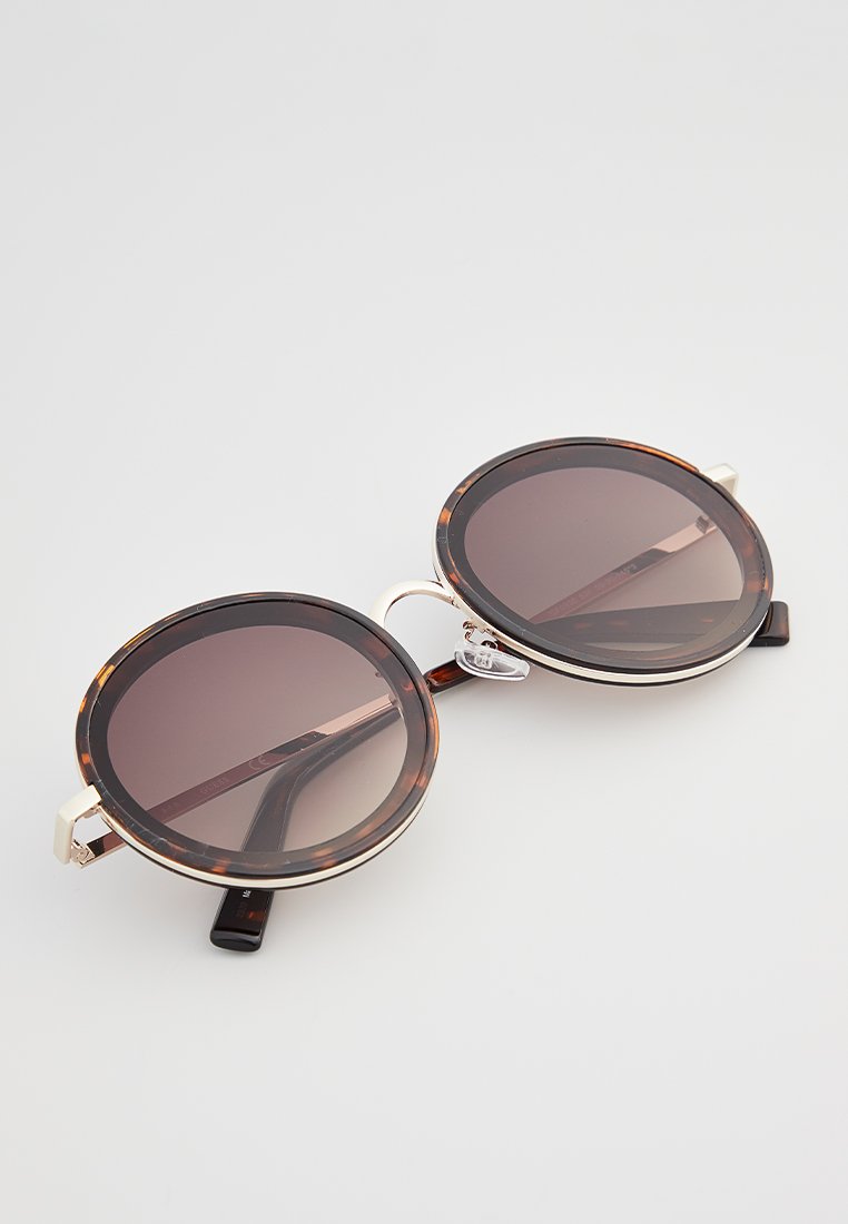 Occhiali da sole rotondi con lenti gradienti scure, montatura a tartaruga, accessori in tono argento e robusti terminali neri per le tempie.