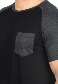 Black short-sleeve t-shirt with dark gray raglan sleeves and a small, textured gray chest pocket. Soft, cotton blend fabric.