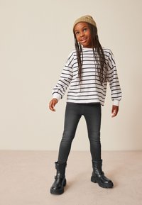 Chemise à rayures noires et blanches à manches longues, jean skinny foncé et bottines noires avec détail de boucle, accompagnés d'un bonnet en tricot beige.