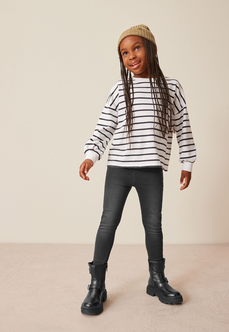 Chemise à rayures noires et blanches à manches longues, jean skinny foncé et bottines noires avec détail de boucle, accompagnés d'un bonnet en tricot beige.
