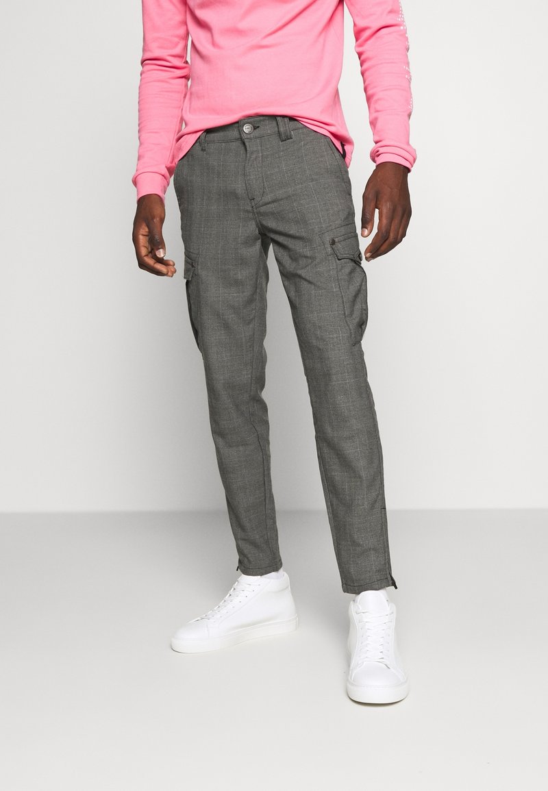 Šedé kárované cargo kalhoty s bočními kapsami, přiléhavý střih a zúžené lemy, kombinované s bílými teniskami a růžovým tričkem s dlouhým rukávem.