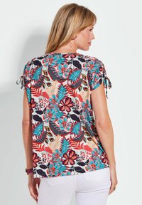 Bloemmotief met korte mouwen top in verschillende kleuren waaronder rood, blauw en groen. Heeft strikaccenten op de mouwen en een losse pasvorm.