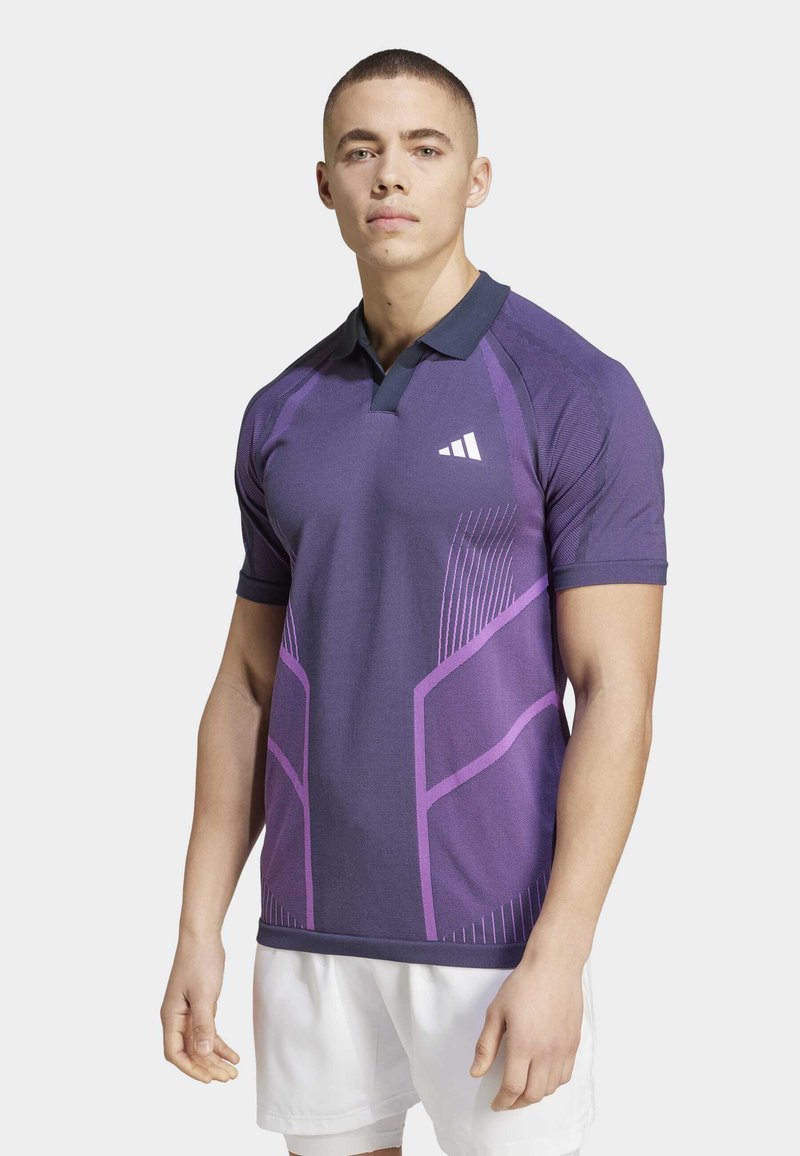 Polo shirt atlético morado con cuello navy, que presenta patrones geométricos en púrpura más claro, mangas cortas y un diseño ajustado.