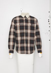 Geruiten shirt in zwart, wit en bruin tinten, met een crèmekleurige sherpa kraag, knoopsluiting aan de voorkant en twee borstzakken.