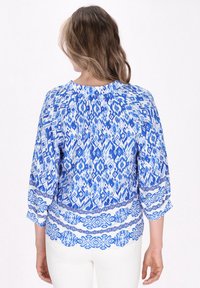 Blusa a maniche lunghe con motivo blu, caratterizzata da disegni intricati in varie tonalità di blu e bianco, e un collo rotondo.