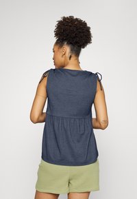 Top sem mangas azul-marinho com cintura franzida, detalhes de alças ajustáveis e textura suave; combinado com calções texturizados verdes claros.