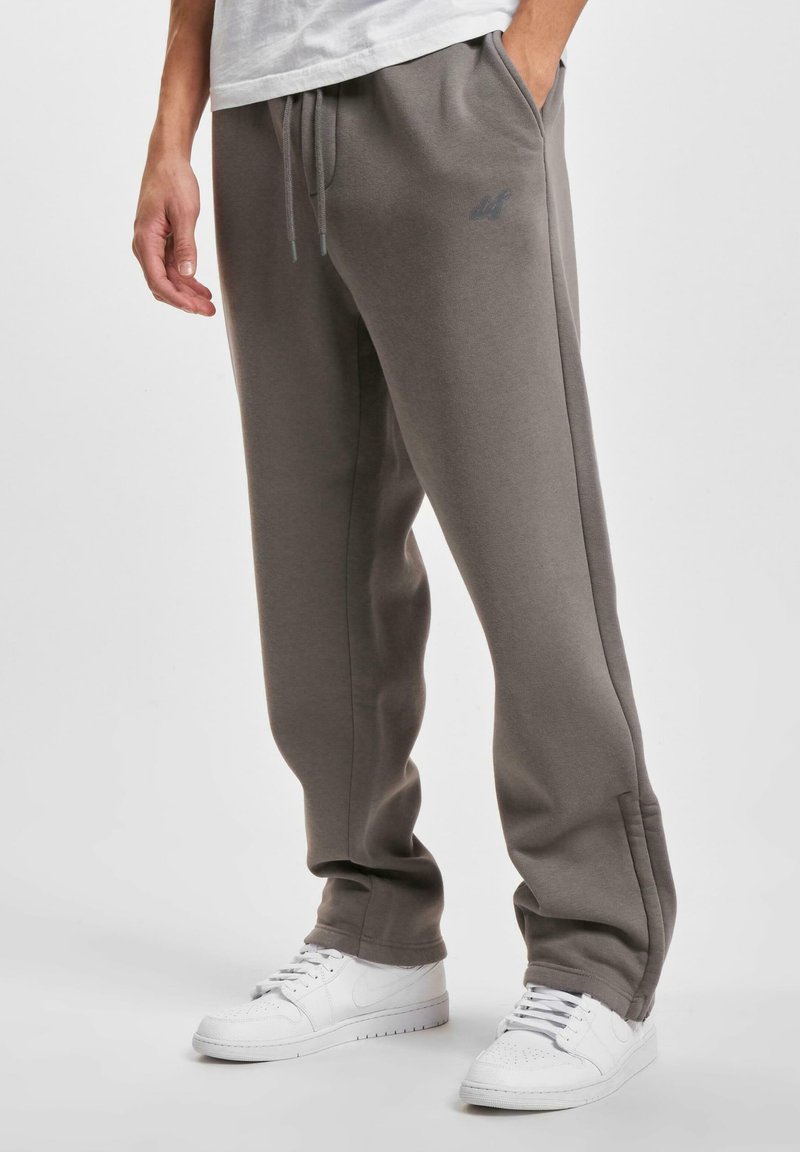 Grå joggebukser med snor i livet, sidelommer og en subtil logo på låret, kombinert med hvite joggesko.