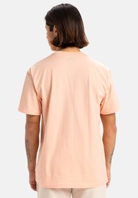 Camiseta de algodón en color melocotón claro, con mangas cortas, un corte relajado y un escote redondo. Textura suave, sin patrones ni gráficos visibles.