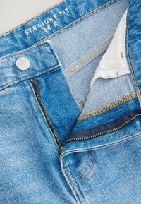 Lichtblauwe denim jeans met een rechte pasvorm. Voorzien van een metalen knoop, ritssluiting en zichtbare stiksels in beige. De voering van de binnenzak is donkerblauw.