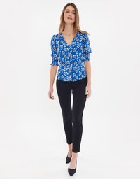 Blusa blu a motivi floreali con maniche corte a sbuffo, design aderente, scollatura a V, abbinata a pantaloni neri slim-fit e tacchi a punta neri.