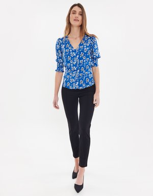 Modrá blůza s květinovým vzorem a krátkými nafouklými rukávy, přiléhavý střih, výstřih do V, v kombinaci s černými slim-fit kalhotami a černými špičatými lodičkami.