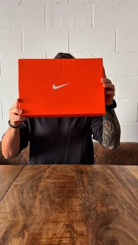Oranž Nike jalatsikarp, millel on valge Nike logo. Taustal on puidust laud, millel on tekstureeritud pind.