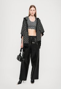 Black cropped jacket with hood, patterned top, and black wide-leg pants. Accessories include a small studded handbag and pointed black shoes.