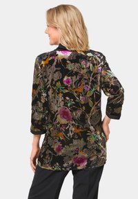 Samt-Tunika mit floralem Muster in den Farbtönen Pink, Lila und Grün auf schwarzem Hintergrund. Dreiviertelärmel und lässige Passform.