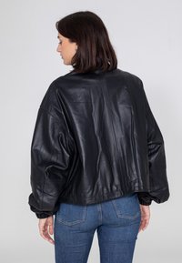 Schwarze Leder-Bomberjacke mit lässiger Passform, überschnittenen Schultern, gerippten Bündchen und cropped Saum, kombiniert mit blauen Jeans.