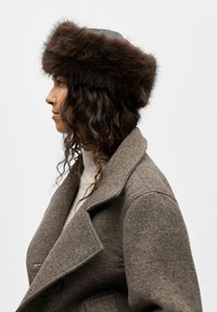 Chapeau en fourrure brune avec un large bord, en fourrure texturée et doublure intérieure lisse de couleur sombre ; porté avec un manteau en tweed gris.
