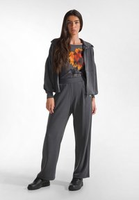 Tuta grigia con felpa con zip e pantaloni a gamba larga, caratterizzata da un top stampato astratto in arancione e rosso. Sneakers nere completano l'outfit.