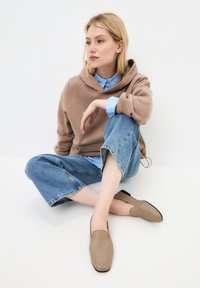 Mocasini din piele bej cu o textură netedă și cusături minime, asortați cu o cămașă albastru deschis și pantaloni din denim scurți.