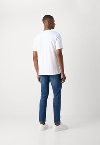 White cotton t-shirt with short sleeves, paired with blue denim jeans and white sneakers. Smooth texture, casual fit, and simple design.