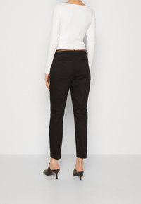 Svarta skräddarsydda byxor med slim fit och avsmalnande ben. Bärs med en figurnära vit långärmad topp och svarta klackskor. Bakifrån visad.