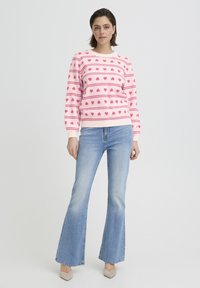 Pull rose clair avec motifs de cœurs, col rond et manches longues. Associé à un jean évasé délavé clair et des talons beige.