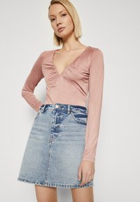 Body à manches longues, rose pâle, avec un décolleté en V et des détails froncés, associé à une mini-jupe en denim bleu clair avec un ourlet effiloché.