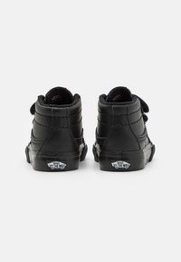Svart høye sneakers med en teksturert lærutside, polstret krage og kontrasterende hvit gummisåle med Vans-logoen.