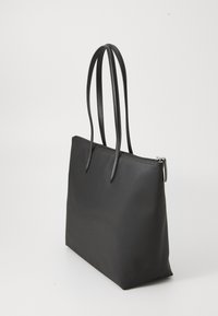 Sac fourre-tout noir avec texture lisse, deux longues poignées et une fermeture zippée en haut. Design rectangulaire simple sans motifs visibles.