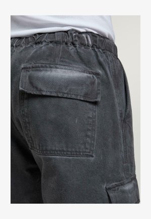 Mørkegrå cargo bukser med elastisk talje, der har en baglomme og en glat tekstur. Nærbillede af side- og bagdetaljer.