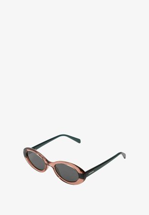 Sonnenbrille mit ovalen Rahmen, transparenter pinkfarbener Vorderseite, dunklen Gläsern und schwarzen Bügeln. Markenname "KOMONO" an der Seite. Glänzende Oberfläche.