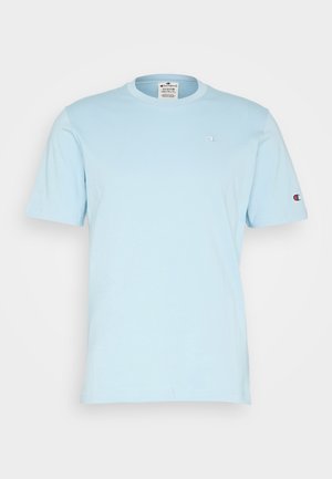 T-shirt Champion bleu clair à manches courtes avec petits logos sur la poitrine et la manche gauche, col rond, présenté sur un fond uni.