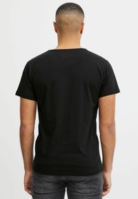 Camiseta negra de manga corta, cuello redondo, fabricada en algodón. Textura suave, diseño ajustado, sin patrones ni acentos visibles en la parte trasera.