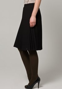 Svart plisserad kjol av texturerat tyg, kombinerad med mörkbruna strumpbyxor och svarta högklackade skor. Mönstrad topp, utan detaljer.